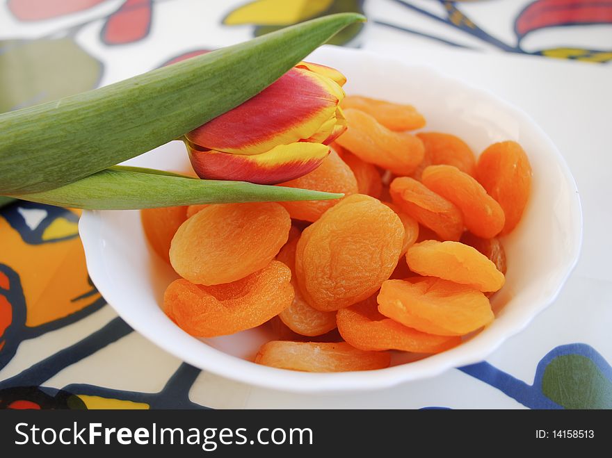 Yellow-red tulip on a plate of dried apricots. Yellow-red tulip on a plate of dried apricots