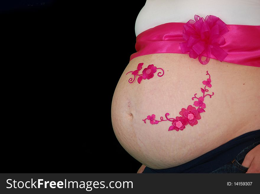 Pregnant belly wrapped in a pink bow and ribbon along with decorative flowers on a black backdrop isolated fushia bright belly button white shirt. Pregnant belly wrapped in a pink bow and ribbon along with decorative flowers on a black backdrop isolated fushia bright belly button white shirt