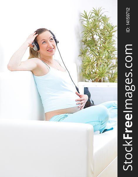 Beautiful piregnant woman sits on a sofa and listens to music