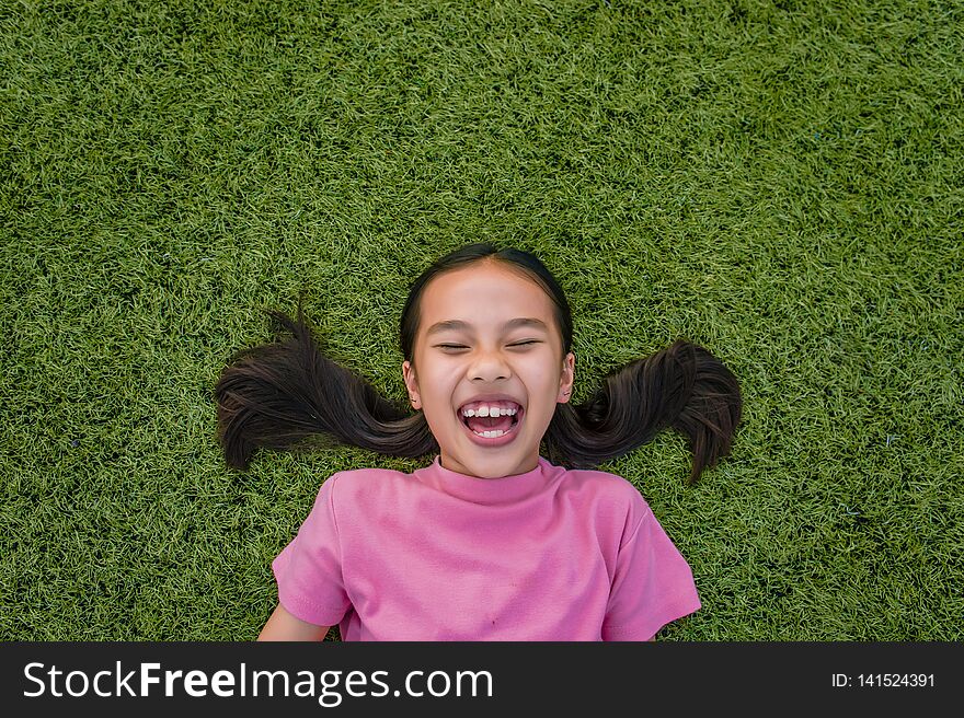 kid asian girl`s lie leisurely on the Lawn floor and smile looking at.