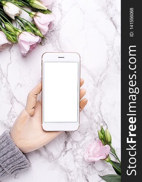 Wooden hand with mobile phone on marble office background with pink flowers