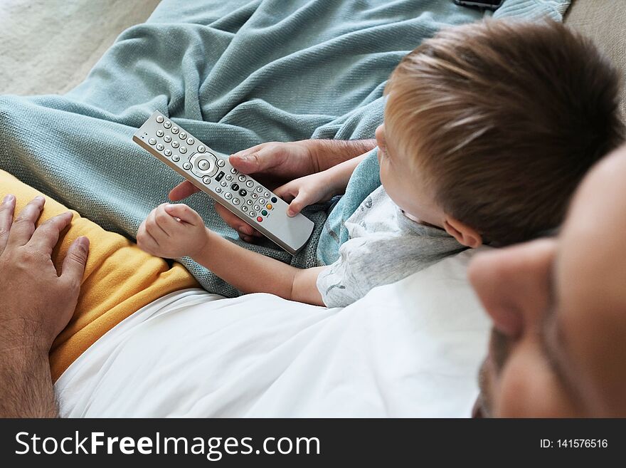 Father and toddler are watching television together and switching the new programme with a remote control