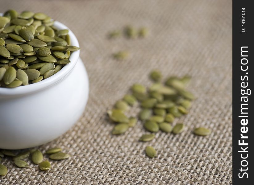 Pumpkin Seeds In A White Pot On A Hessian Cloth. Pumpkin Seeds In A White Pot On A Hessian Cloth