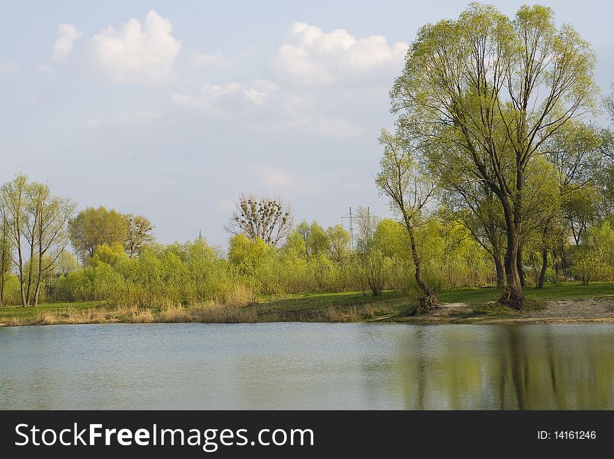 Landscape near the lake at good spring day with trees and bushes with young leaf and blue skies with clouds. Landscape near the lake at good spring day with trees and bushes with young leaf and blue skies with clouds