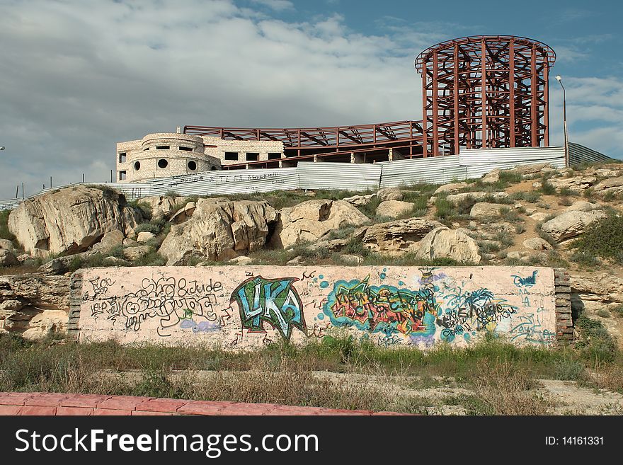 A wall with graffiti graphics. In the background is an unfinished building. A wall with graffiti graphics. In the background is an unfinished building.