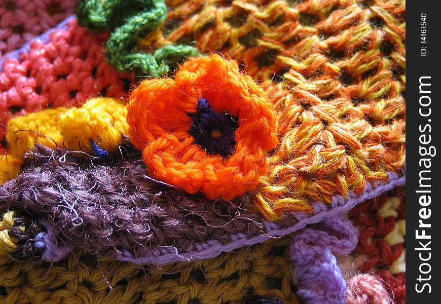 Closeup of an orange crocheted flower with a multi-colored crochet fabric background. Closeup of an orange crocheted flower with a multi-colored crochet fabric background.