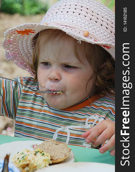 Pretty little girl in hat eating by folk. Pretty little girl in hat eating by folk