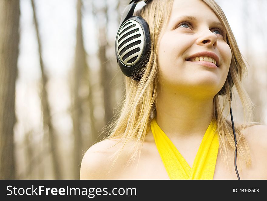 Blond woman smiling listening to music in headphones outdoors. Blond woman smiling listening to music in headphones outdoors