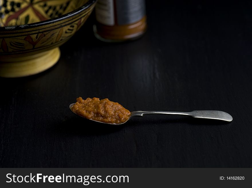 A Spoonful of Harissa Paste In Front of A Moroccan Dish On A Slate Worktop,. A Spoonful of Harissa Paste In Front of A Moroccan Dish On A Slate Worktop,