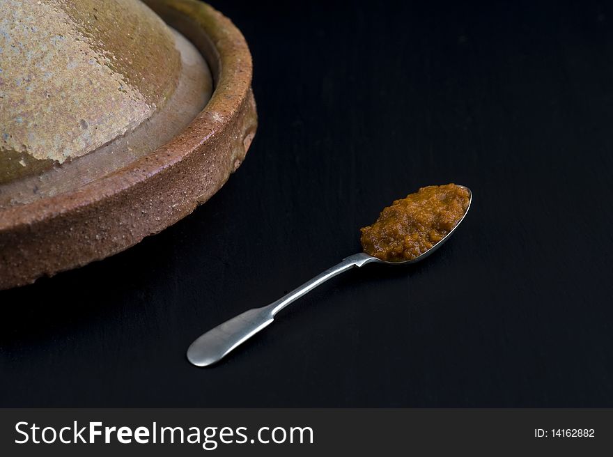 A Spoonful of Harissa Paste Near A Tagine On A Slate Background