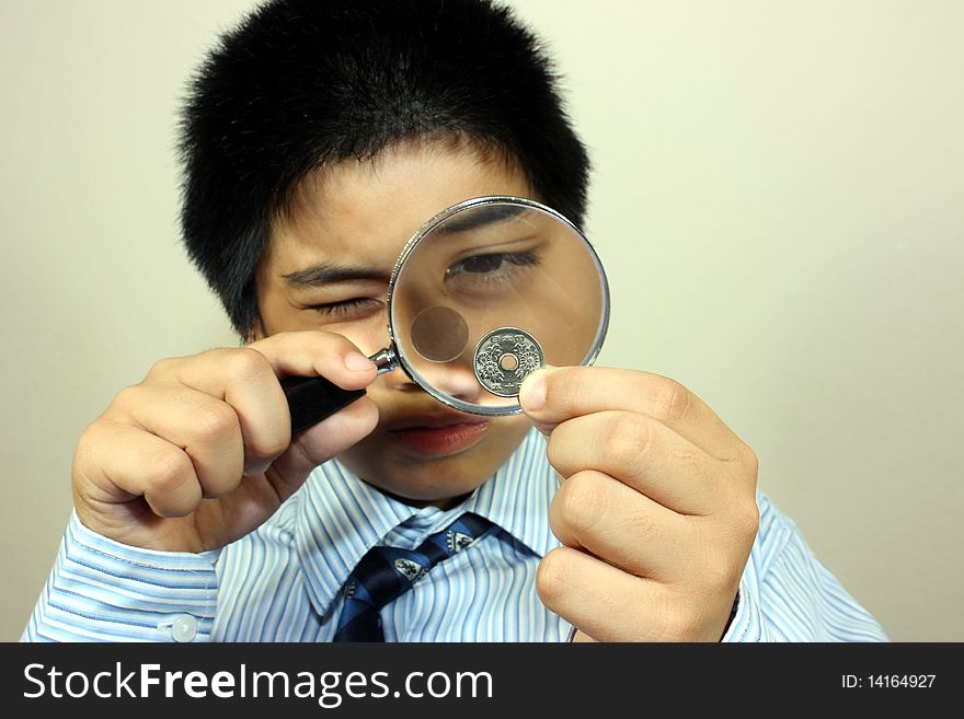 An asian boy in a suit examining a coin with a magnifying glass. An asian boy in a suit examining a coin with a magnifying glass
