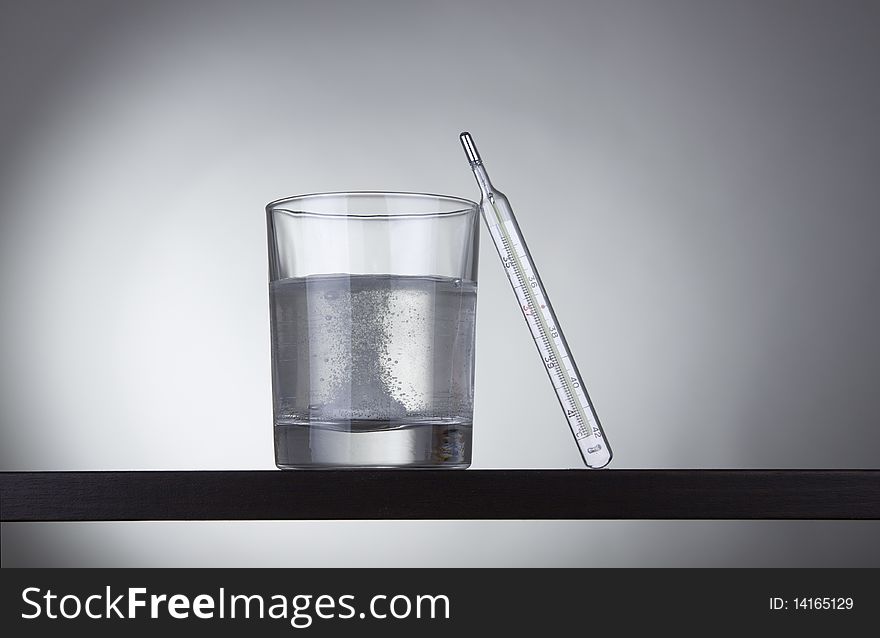 Glass with thermometer on gray background