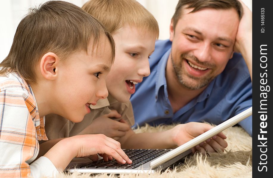 Two brothers playing on a laptop next to his father