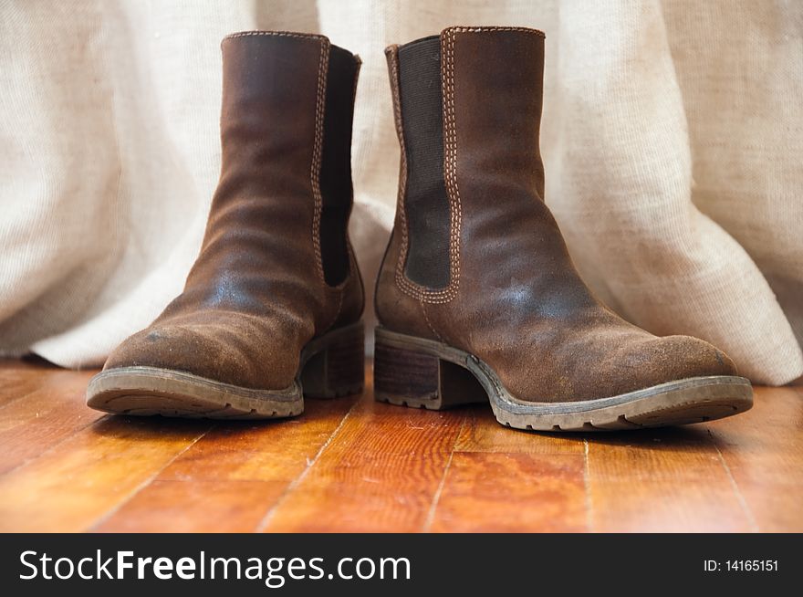 A pair of dirty workboots against a background of a linen drape and on a rustic wood floor. A pair of dirty workboots against a background of a linen drape and on a rustic wood floor.