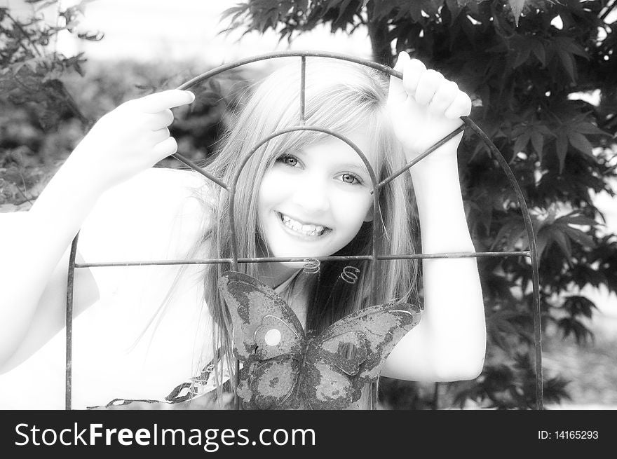Happy young girl smiling behind wire trellis with butterfly high contrast. Happy young girl smiling behind wire trellis with butterfly high contrast