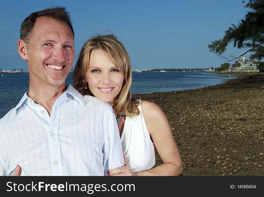 Husband and wife lifestyle image on the shoreline of Miami's Biscayne Bay with skyline and bridge in the background.