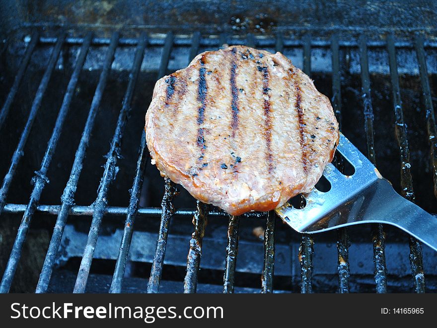 Spatula flipping hamburger on grill