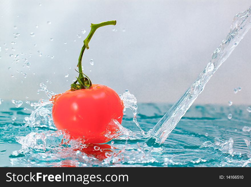 Red tomato with green stalk and splash water over white background