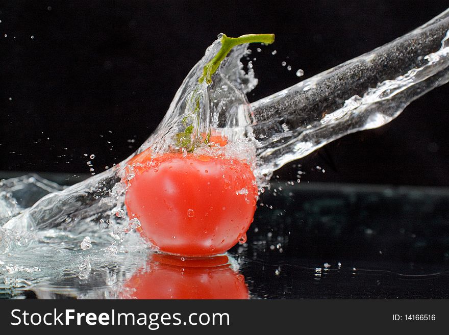 Red tomato with green stalk and splash water over black background