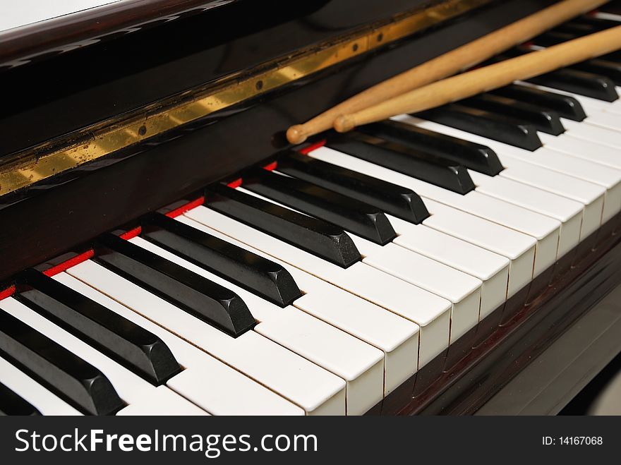 Diagonal shot of drum sticks on piano keyboard