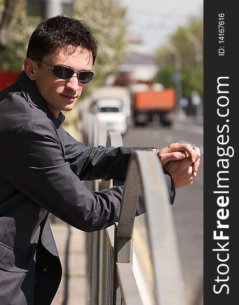 Young guy in black sunglasses waiting for someone near the road in the middle of a day. Young guy in black sunglasses waiting for someone near the road in the middle of a day