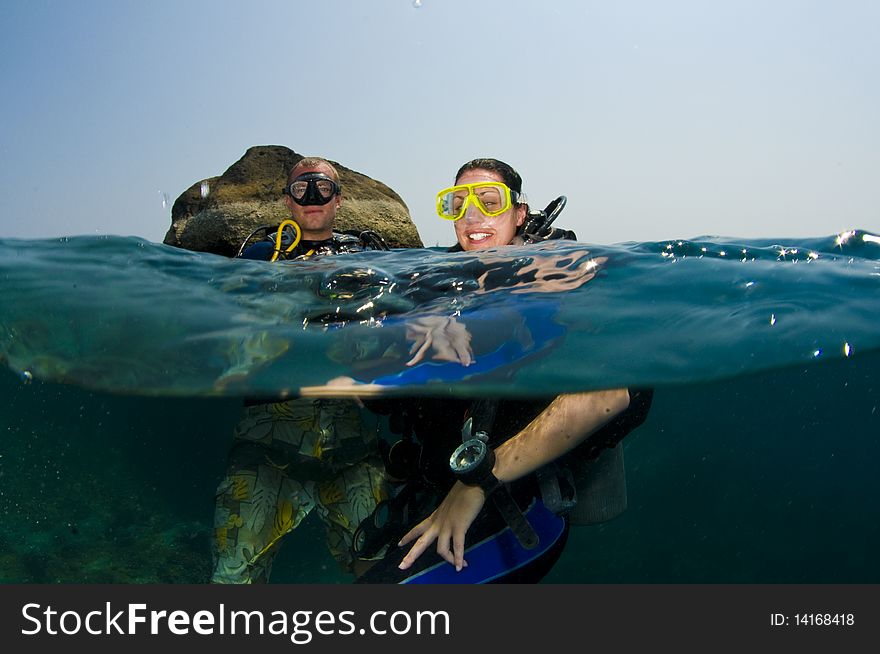 Over/under shot of couple of scuba divers. Over/under shot of couple of scuba divers