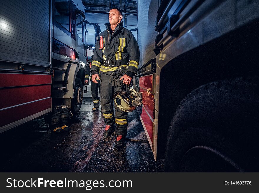 Full-length portrait of two brave firemen in protective uniform walking between two fire engines in the garage of the