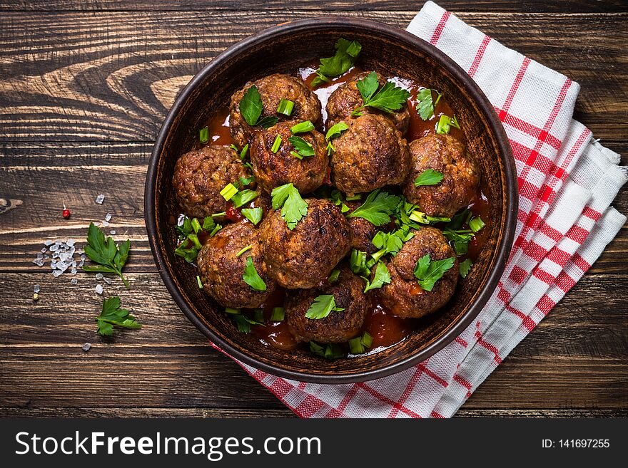 Meatballs in tomato sauce and greens on dark wooden table. Rustic style. Top view. Meatballs in tomato sauce and greens on dark wooden table. Rustic style. Top view.