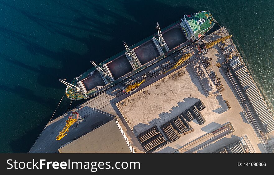 Top view of the port harbor with cargo ship on the pier and loading and unloading area, storage area