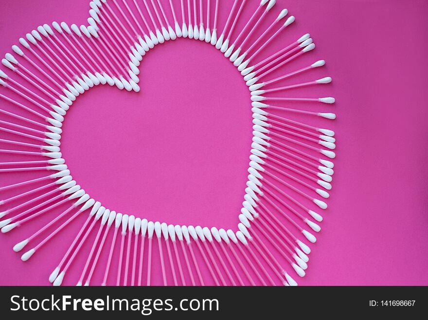 Cotton buds laid out in the shape of a heart on a pink background