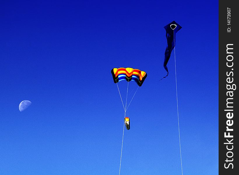 Two colorful kites set against deep blue sky with half moon in background