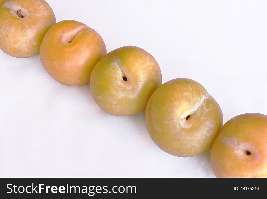 A row of five yellow plums on a white background