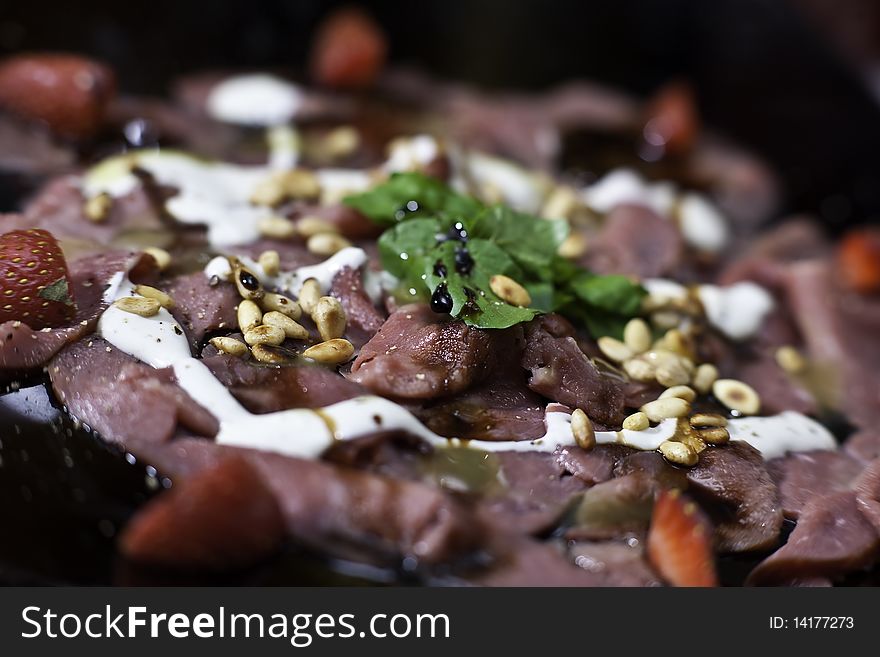 Springbok carpaccio with a white sauce, strawberries and nuts on a black plate