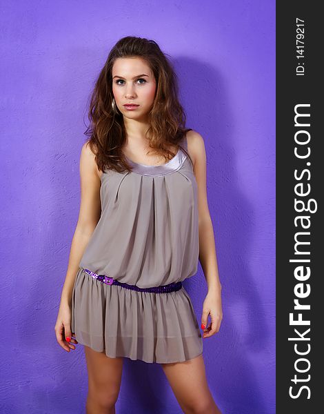 Shot of young and beautiful woman wearing beige dress and lilac glitter belt on lilac background. (Professional makeup and hair style)