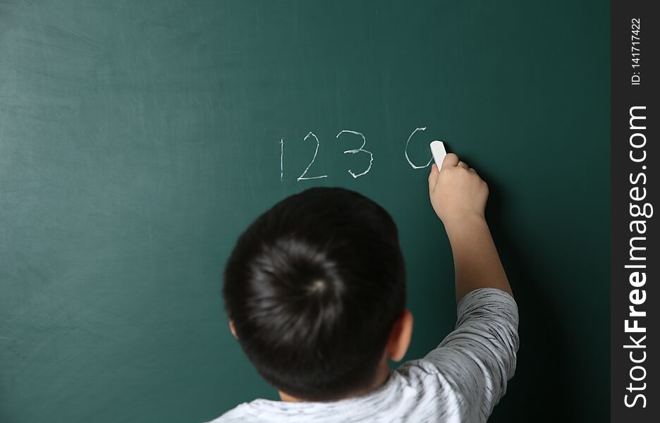 Child writing math sum on chalkboard.