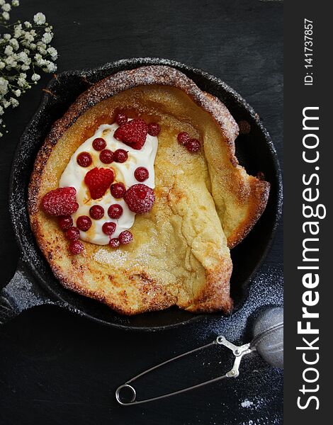 Dutch baby pancake on black background with red fruits and cream