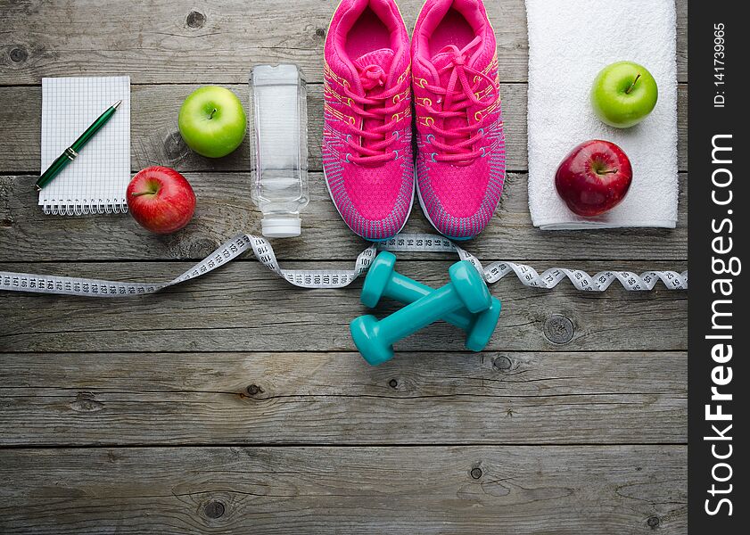 Sneakers Dumbbells Bottle Of Water And Apple On Wooden Table