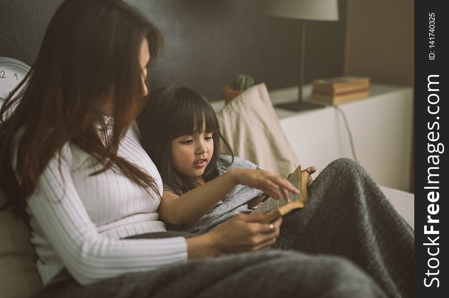 Mother and daughter reading book at home in the bedroom.