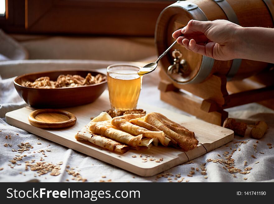 Mead and pancakes. Russian dish for Shrove Tuesday. Farewell to winter. The hand in the frame. Honey from a spoon dripping on pancakes. Mead and pancakes. Russian dish for Shrove Tuesday. Farewell to winter. The hand in the frame. Honey from a spoon dripping on pancakes