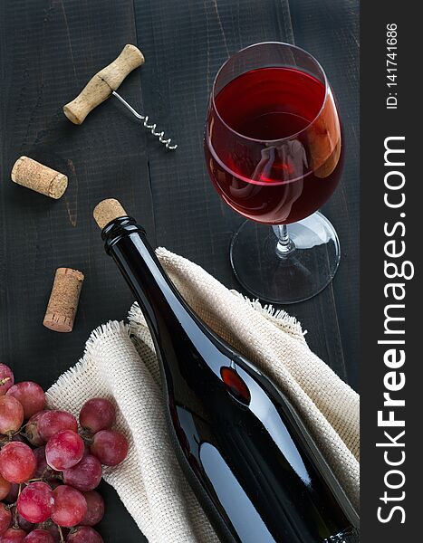 Bottle of wine, wine glass, grapes and corkscrew on dark background