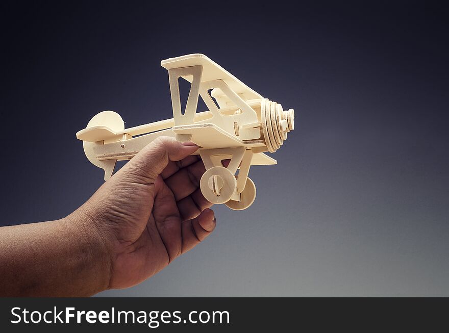 Hand holding toy wooden retro airplane on dark background for travel concept