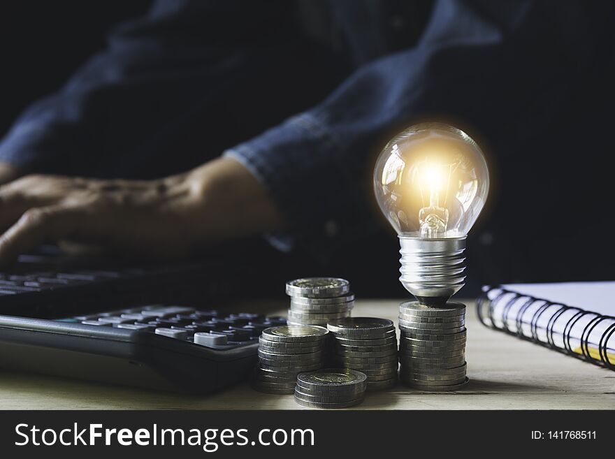 Man working with a light bulb on stack of coins for business and accounting concept