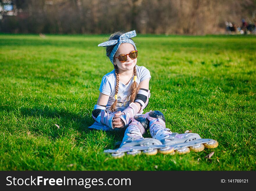 Cute curly girl funny sitting in roller skates and sunglasses and looking at the camera