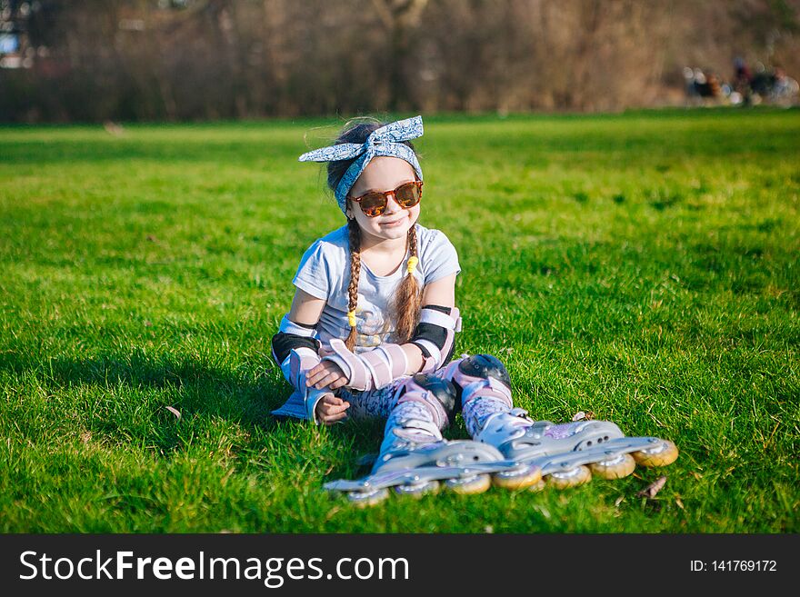 Cute curly girl funny sitting in roller skates and sunglasses and looking at the camera