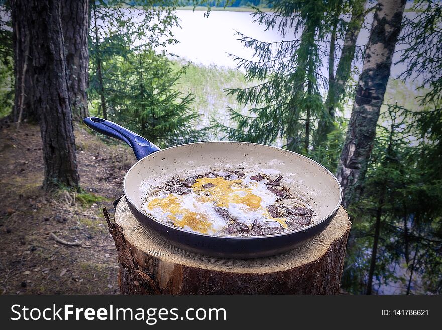 Fried eggs lie on the pan cooked in nature, in a hike breakfast tourism forest bonfire stump lake river travel yellow cholesterol cooking protein yolk white food healthy diet hot oil close-up iron fresh top