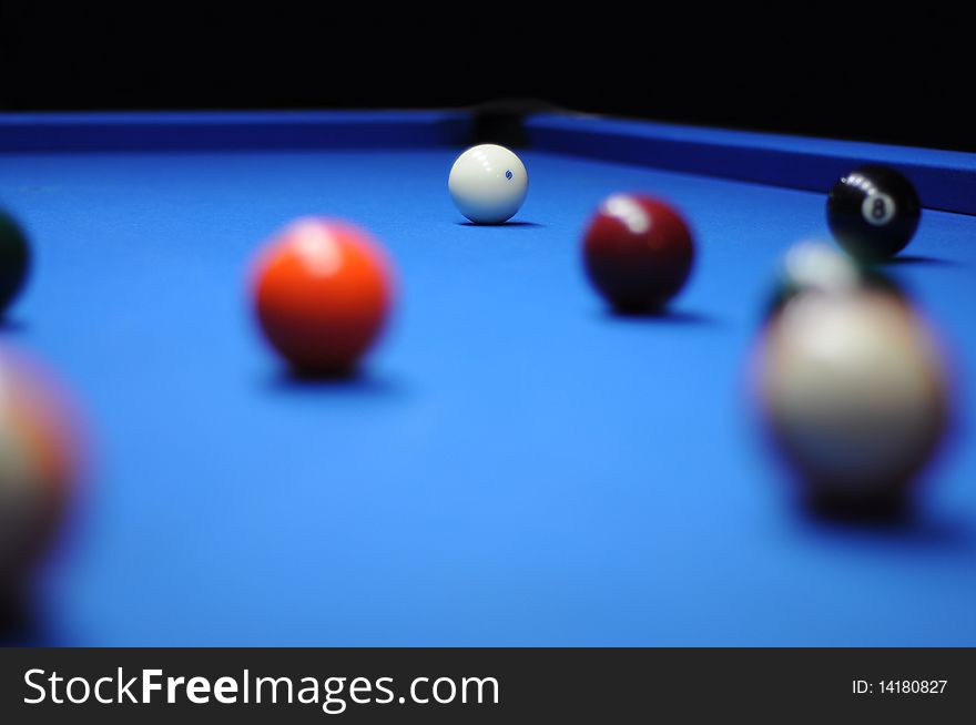 Several billiard balls on a blue table, focusing on the white ball