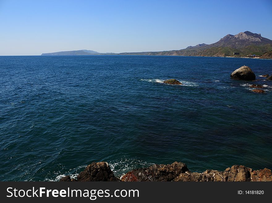 Seascape - a beautiful beach, sea and sky. In the foreground stones from the vent of an ancient volcano karadag. Seascape - a beautiful beach, sea and sky. In the foreground stones from the vent of an ancient volcano karadag