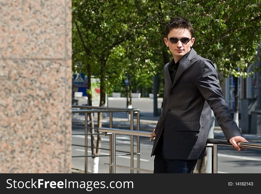 Young businessman in sunglasses leans on handrails. Young businessman in sunglasses leans on handrails