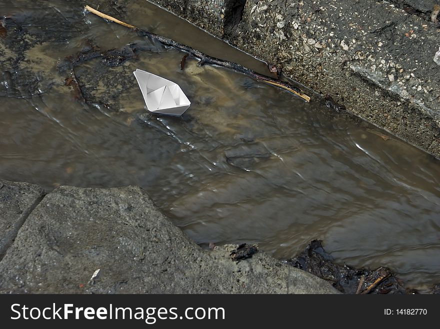 A white paper toy-ship swims on a brook on an asphalt