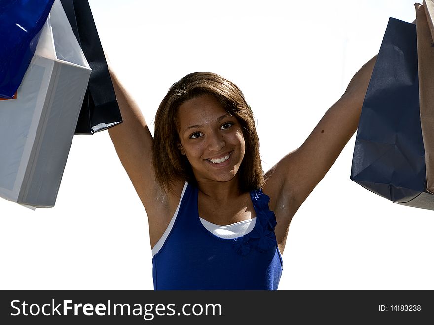 Multi race teenage girl with her arms holding up several shopping bags, smiling, happy shopper, accent of sun highlights along side of cheek. wearing a bright blue layered white tank top. white back ground. Multi race teenage girl with her arms holding up several shopping bags, smiling, happy shopper, accent of sun highlights along side of cheek. wearing a bright blue layered white tank top. white back ground.